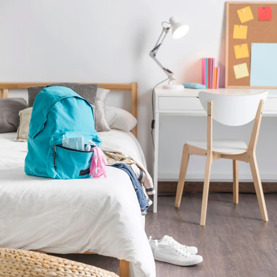 기숙사 방 침대 위 백팩과 옷가지
