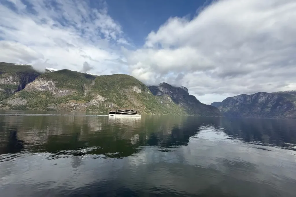 노르웨이 아우를란 피오르드의 푸른 물 위를 유유히 지나가는 작은 유람선과 거대한 빙하 계곡 풍경.