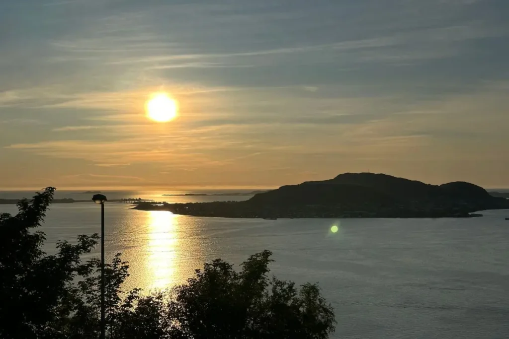 노르웨이 올레순의 악슬라 전망대에서 바라본 백야의 석양. 주황빛과 분홍빛으로 물든 하늘 아래 올레순 시내와 주변 섬, 피오르드가 펼쳐져 있다.