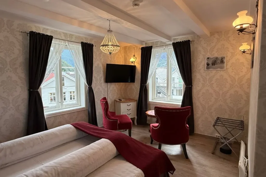 노르웨이 방스가르덴 호텔 객실의 앤티크한 나무 테이블과 의자 세트가 창가에 놓여 있는 모습.